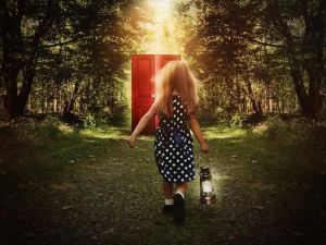 A little child is walking in the woods holding a light and looking at a glowing red door on the path for a mystery or imagination concept.